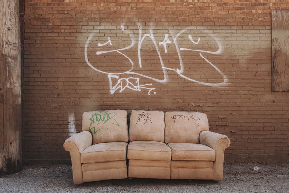 A worn-out sofa sits against a graffiti-covered brick wall in an urban alley.